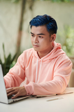 Portrait of serious young man working on laptop at home reading brief from client