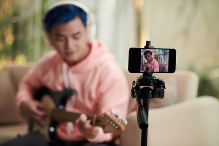 Talented young man recording himself playing guitar on smartphone