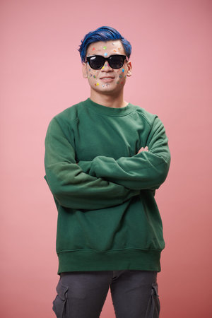 Smiling young man in sunglasses and green sweater crossing arms and looking at camera