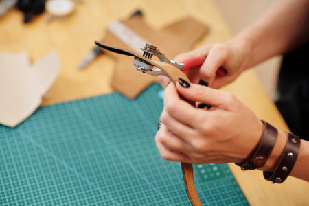 Hands of craftsperson perforating leather belt with special toolの写真素材