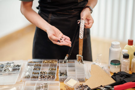 Closeup image of craftsperson choosing eyelets for leather belt she is working on