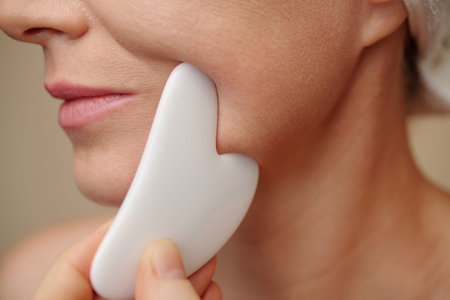 Closeup image of middle-aged woman using gua sha when massaging lower part of her face
