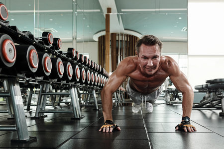 Strong fit man doing push-up on gym floor when working on chest muscles
