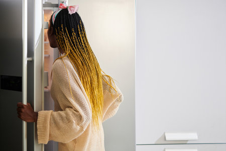 Hungry young woman opening fridge to taking something to eatの写真素材