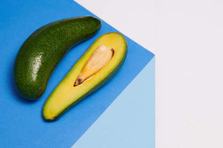 Long avocado and a half on blue table, healthy eating concept