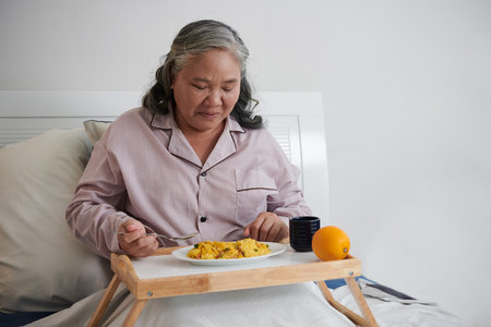 Senior woman on cotton pajamas eating lunch in bedの写真素材