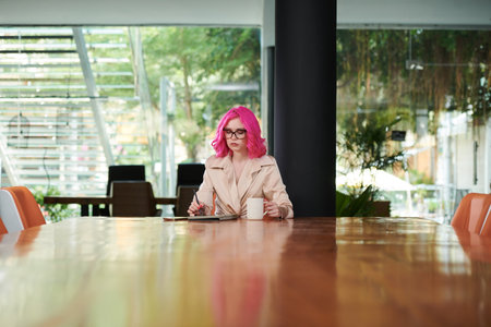 Serious young female entrepreneur drinking coffee when reading news article on tablet computerの写真素材