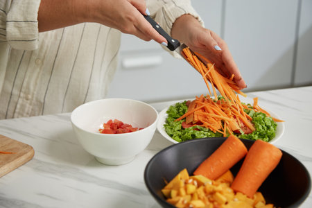 Hands of woman putting julienned carrots in pile onto lettuce leaves