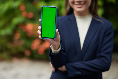 Cropped image of businesswoman showing smartphone with green screenの写真素材