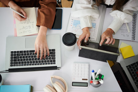 Top view of businesswomen working in team over project sitting at table with gadgets and documents