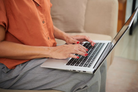 Close-up of young woman surfing the net on laptop sitting on sofa in the living roomの写真素材