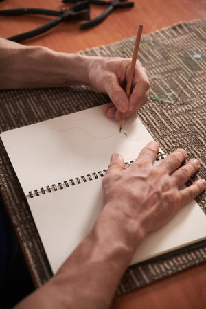 Vertical image of man drawing sketch with pencil in his notebook sitting at tableの写真素材