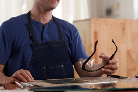 Worker using protective glasses at his work while working at table with piece of glassの写真素材