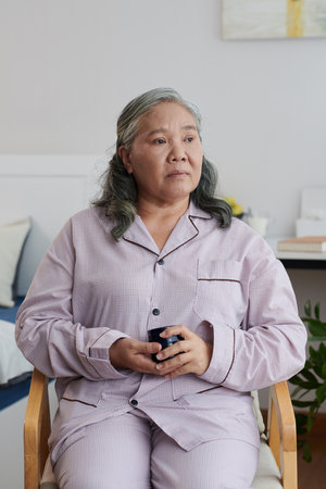 Senior woman sitting in wheelchair, drinking cup of green tea and looking awayの写真素材