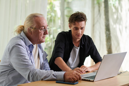 Senior man asking grandson to help with sending e-mailの写真素材