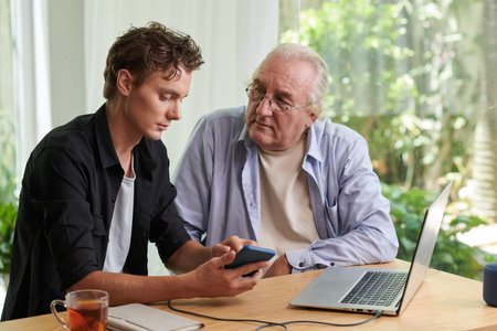 Senior man listening to grandson explaining how to use application on smartphoneの写真素材
