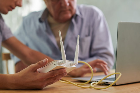 Closeup image of young man setting wi-fi router in apartment of his senior fatherの写真素材