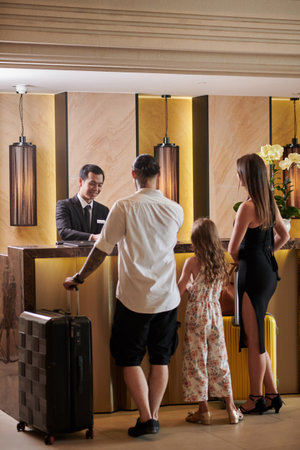 Married couple with preteen daughter standing at hotel receptionの写真素材