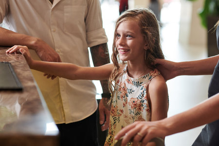 Excited preteen girl checking in at hotel reception with her parents for the first timeの写真素材