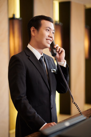 Luxurious hotel receptionist in elegant suit answering phone callの写真素材