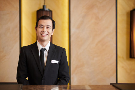Portrait of positive Asian hotel receptionist with badge on his suitの写真素材