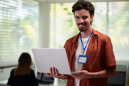 Portrait of positive software developer with laptop in hands standing in officeの写真素材