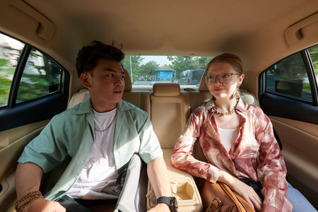 Diverse young couple chatting when sitting on backseat of taxi carの写真素材