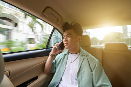 Young Vietnamese man talking on phone when riding taxi car to workの写真素材