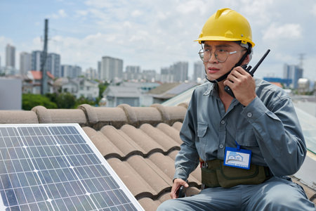 Contractor standing on roof next to solar panel and talking using walkie-talkie