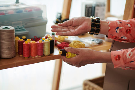 Hands of seamstress choosing threads for clothing item she is working on