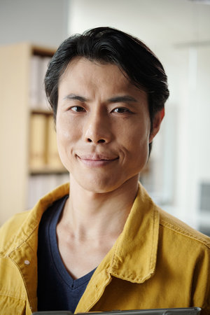 Portrait of cheerful Asian man in mustard shirt standing in officeの写真素材