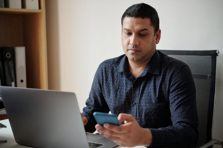 Serious businessman reading text message when working on laptop at office desk