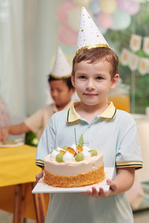 Portrait of preteen boy in party hat carrying birthday cakeの写真素材