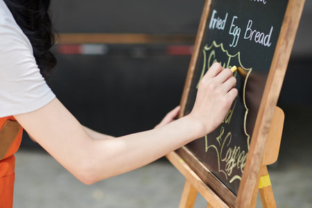 Closeup image of small business owner writing menu of street food cafe on chalkboardの写真素材