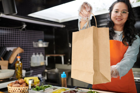 Smiling food truck worker giving paper bag with order and looking at camera