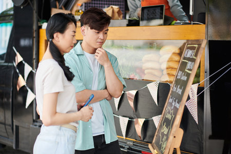 Pensive young people looking at food truck menu deciding what to orderの写真素材