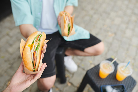 Couple eating sandwiches and drinking soda when having lunch in parkの写真素材