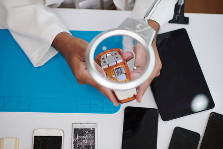 Technician using magnifying glass when examining broken feature phoneの写真素材