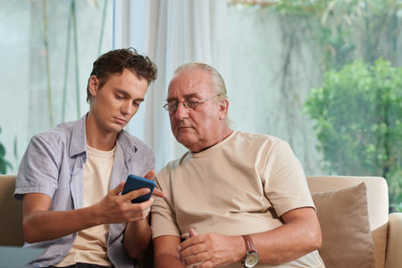 Young man showing senior man how to send text messages, voice messages and stickers in messengerの写真素材