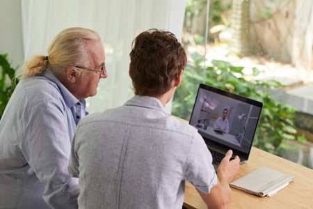 Young man showing senior father how to use telemedicine service