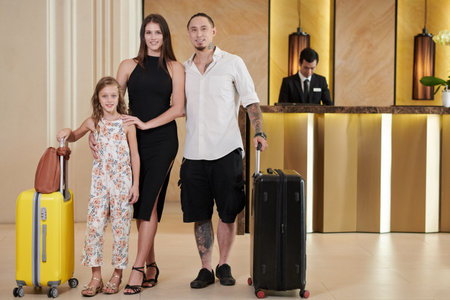 Happy father, mother and preteen girl with suitcases standing in hotel hallの写真素材