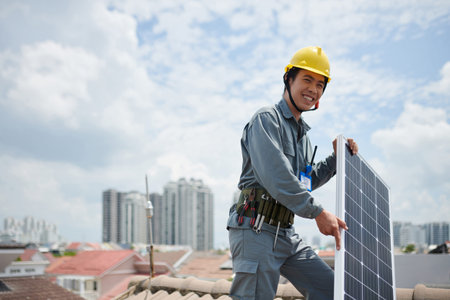 Positive Vietnamese contractor standing on roof with solar panel