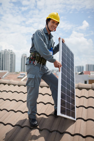 Cheerful builder standing on roof with photovoltaic panel