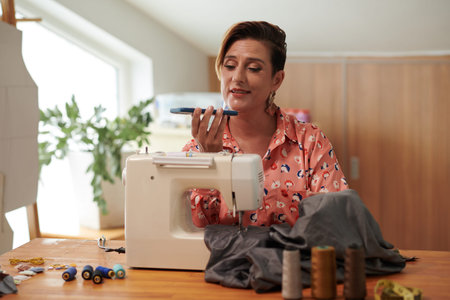 Positive seamstress answering voice messages from client when sewing gown