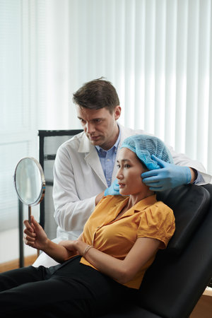 Cosmetologist giving mirror to patient to check result of injectionsの写真素材