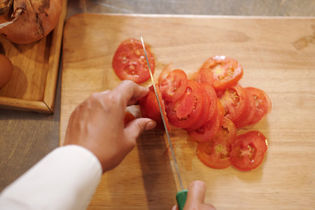 Closeup image of cook cutting fresh tomatoes in thin slicces, view from aboveの写真素材