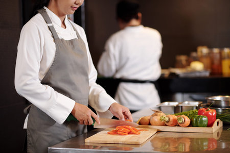 Female chef cutting tomatos when cooking salad in hotel kitchenの写真素材