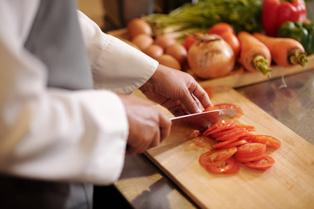 Closeup image of cook cutting fresh tomatoes in thin slices