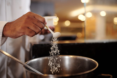 Closeup image of chef putting spoon of salt in big saucepanの写真素材
