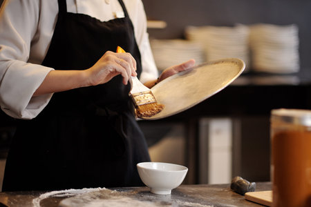 Pizza maker using synthetic brush when covering tray with thin layer of vegetable oilの写真素材